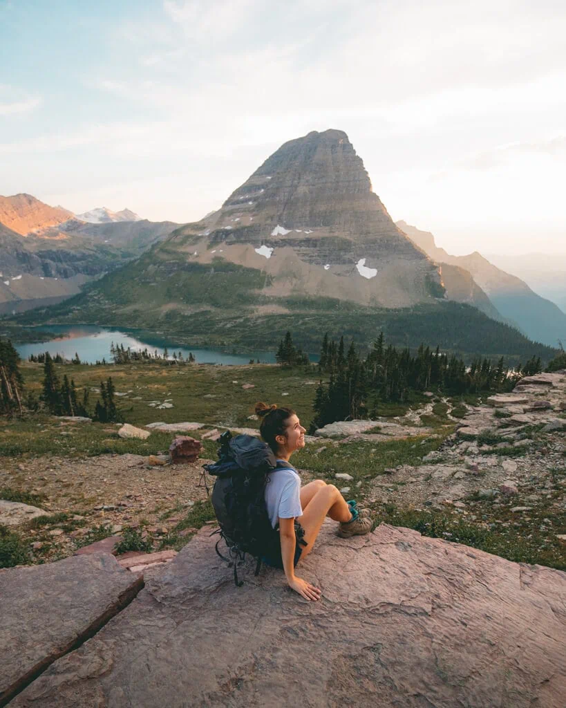 female hiker watching a pink sunset over Hidden Lake Overlook Trail in glacier national park montana