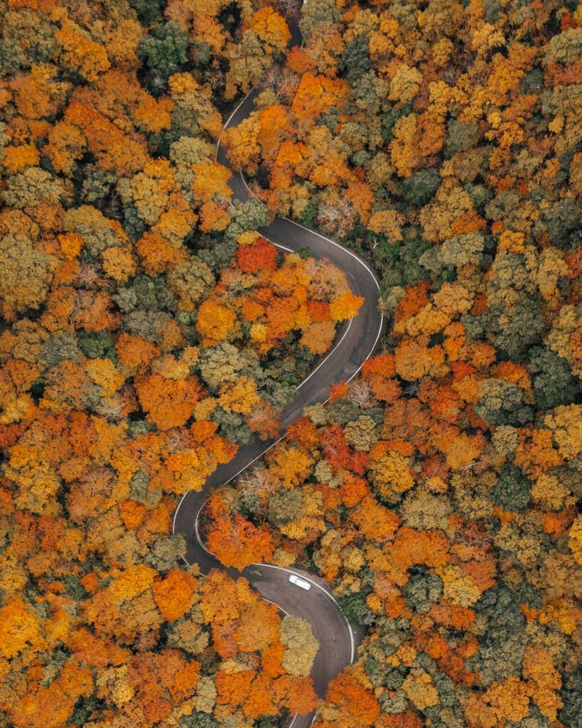drone shot of a windy road with fall colors in smugglers notch state park vermont